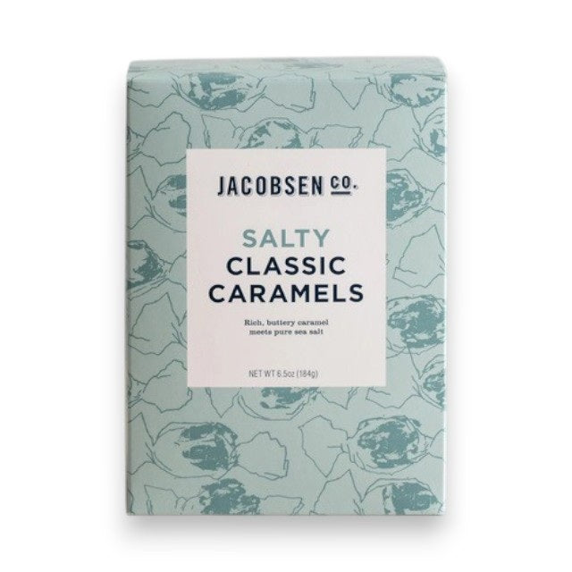 A light blue box of JACOBSEN SALT CO. JACOBSEN SALT - SALTY CARAMELS BOX, featuring a patterned design and product label on the front, rests on a light surface.