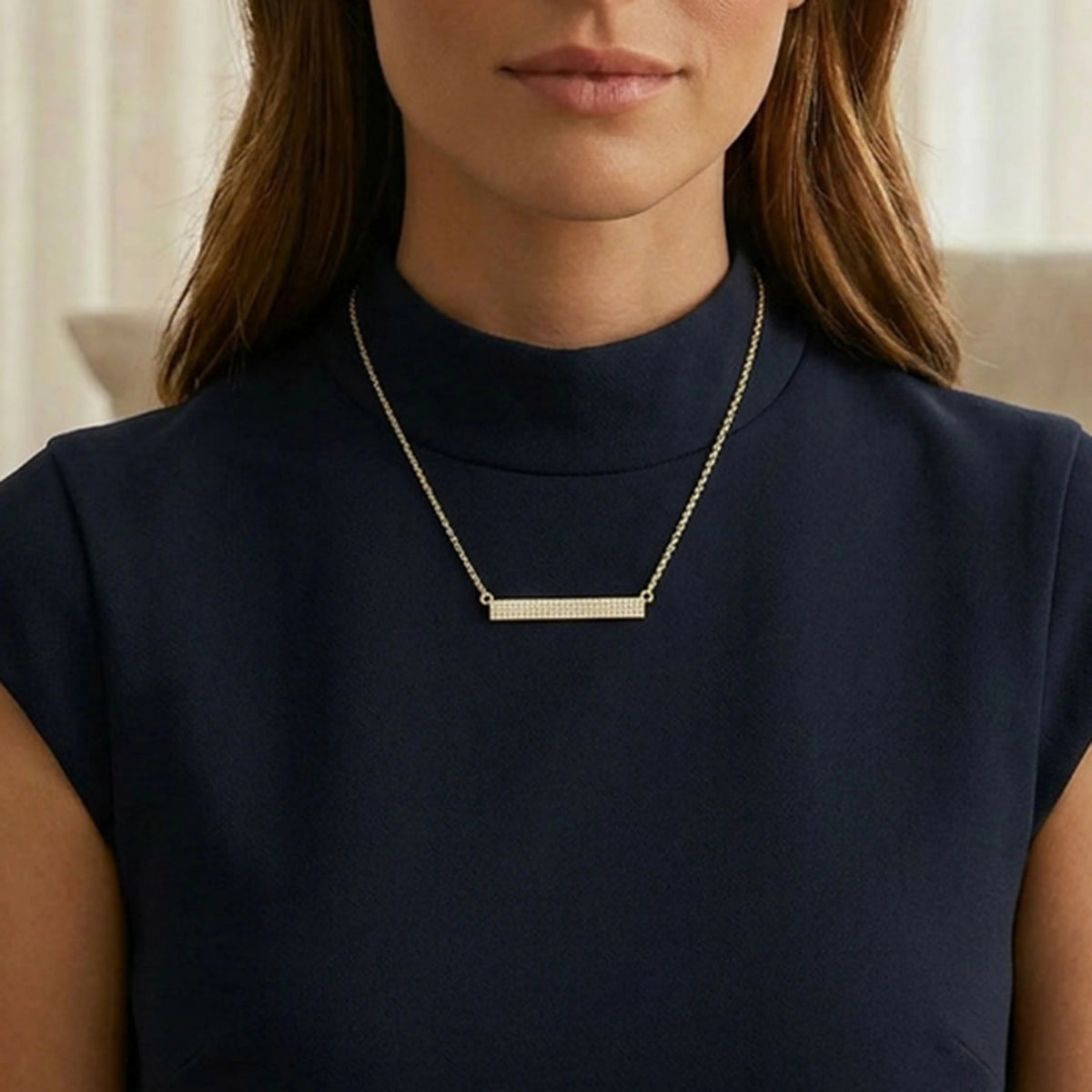 The ELLA STEIN - TELL ME STRAIGHT PENDANT NECKLACE by ELLA STEIN features a gold chain and a horizontal rectangular gold-plated pendant adorned with rows of small, sparkling stones. Displayed against a plain white background, this elegant stainless steel jewelry piece perfectly combines durability with timeless style.