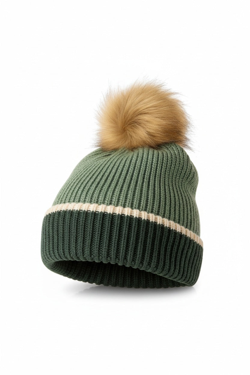 The MERSEA Montauk Colorblock Beanie in Eden showcases a green ribbed knit design with a cream stripe and dark green edge, finished with a large brown faux fur pom-pom—an ideal cold-weather accessory from MERSEA, presented on a plain white background.