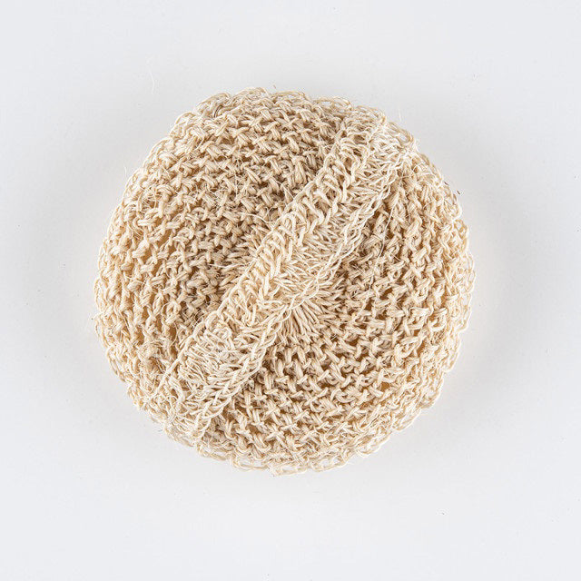 A round, woven beige loofah pad, the BAUDELAIRE - SISAL SPONGE by BAUDELAIRE, handmade in Colombia from natural sisal fiber, is shown on a plain white background. The loofah has an attached hand strap for easy grip and use, featuring a textured, mesh-like surface perfect for exfoliation.
