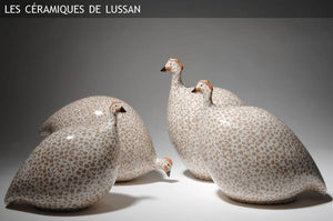 Four large ceramic pecking French guinea fowl in white with black spots are displayed against a neutral background. The text "Les Céramiques de Lussan" appears at the top left corner, showcasing exquisite handmade pottery from France.