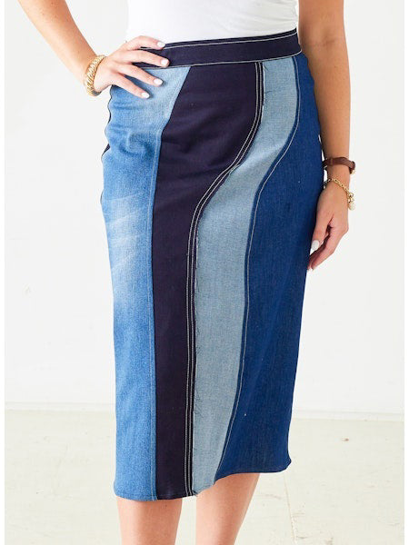 The MERSEA PRISM PATCHWORK DENIM SKIRT features multiple blue shades, contrast stitching, and a fitted knee-length, high-waisted silhouette—perfectly styled with a white top and bracelets for a bold statement.