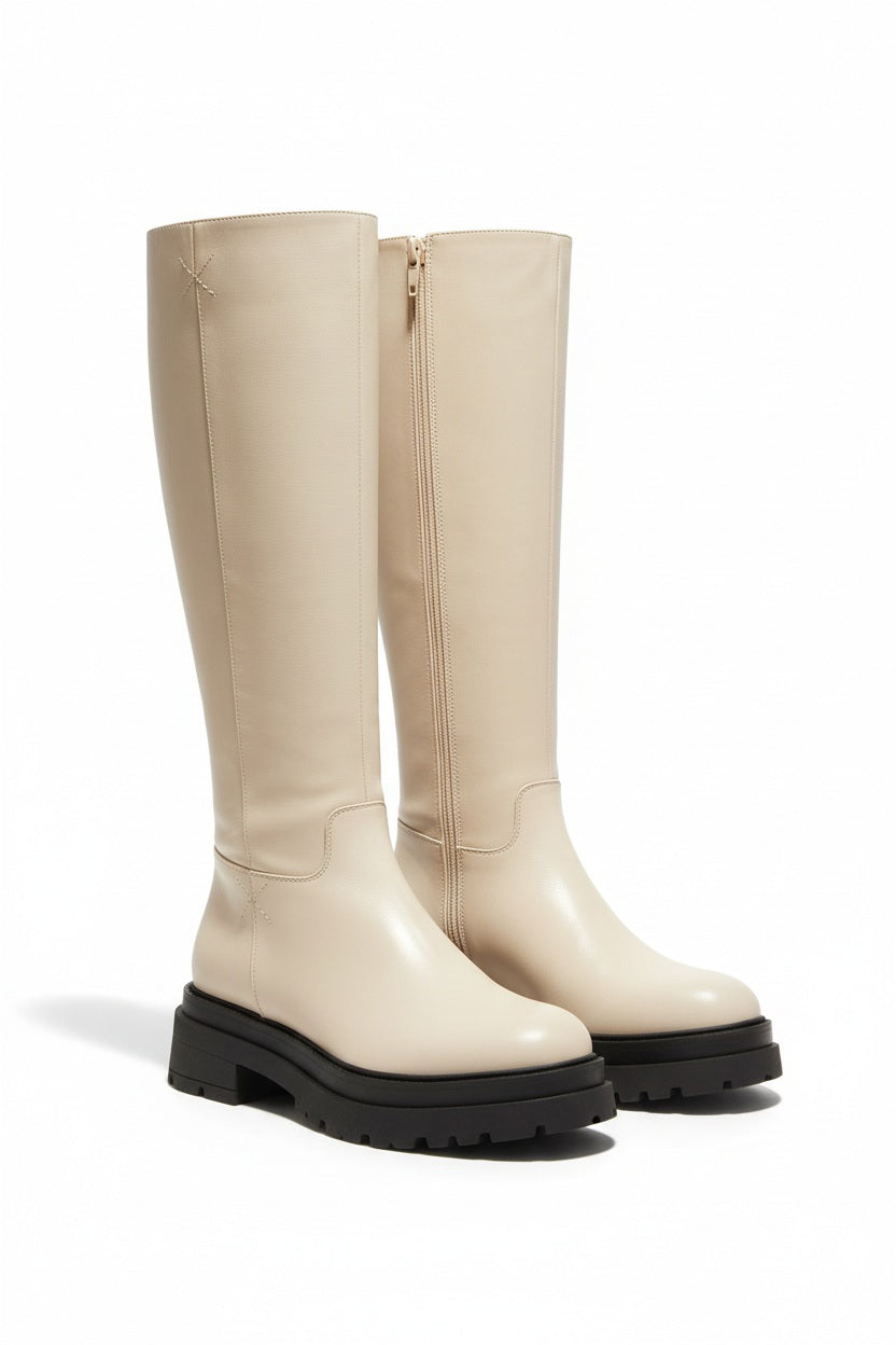 A person stands against a plain white background wearing the TALL LEATHER BOOT by MICHELE LOPRIORE—crafted from genuine leather, featuring chunky soles, and made in Italy.