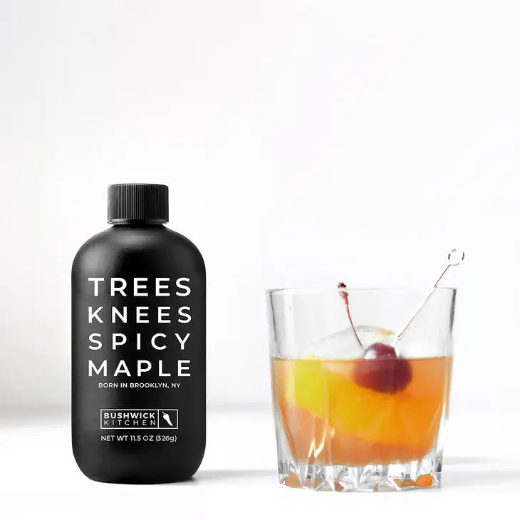 A black bottle with minimalistic design and white text that reads &quot;TREES KNEES SPICY MAPLE, BORN IN BROOKLYN, NY.&quot; Below the text is the &quot;BUSHWICK KITCHEN&quot; logo, along with &quot;NET WT 12.5 OZ (354g).&quot; The bottle features a screw cap. This BUSHWICK KITCHEN - &#39;TREES KNEES&#39; Spicy Maple Syrup is infused with habanero for the perfect kick.