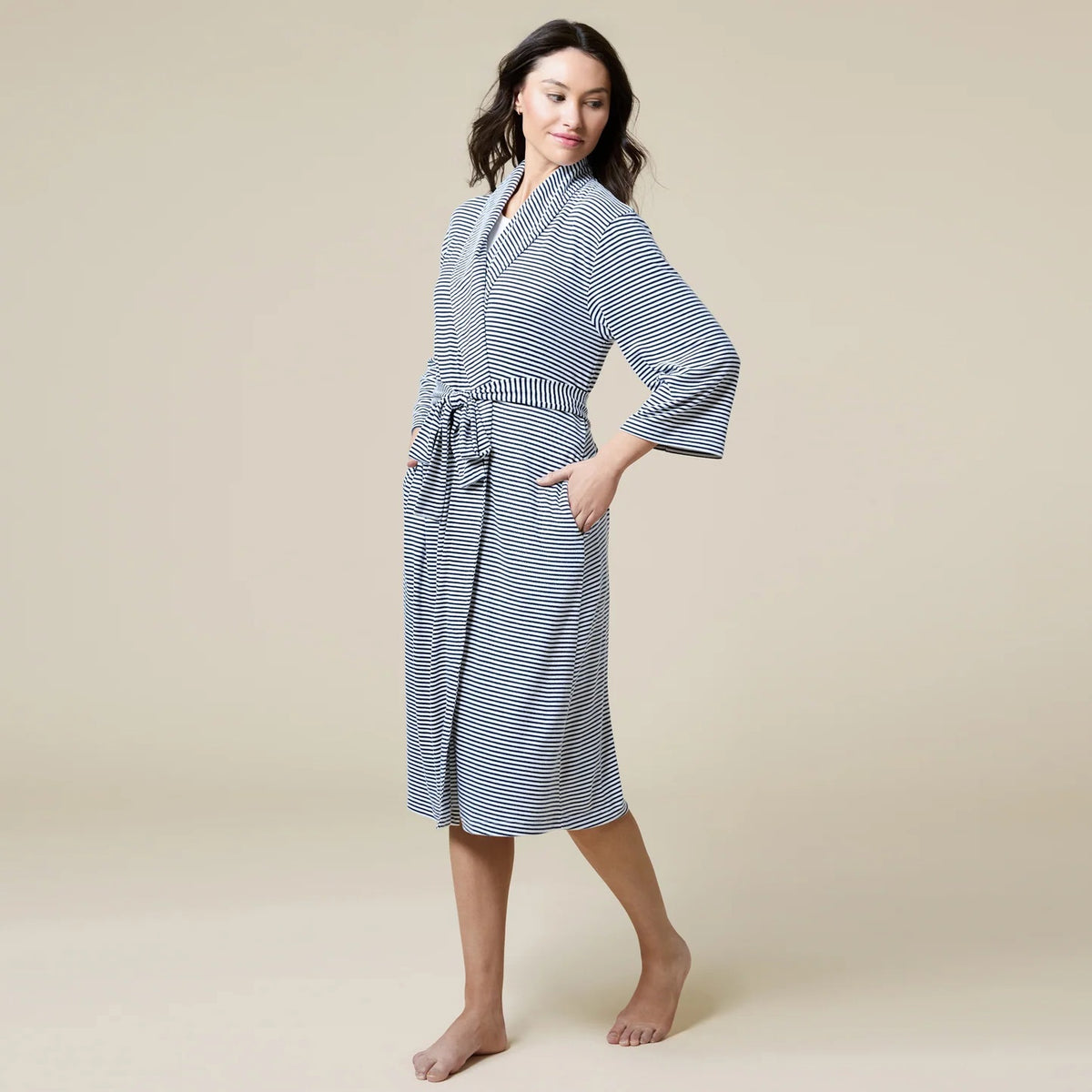 A woman wears a SOFTIES - DREAM SHAWL COLLAR ROBE in pink and white stripes, featuring a shawl collar, a tie waist, and three-quarter length sleeves.