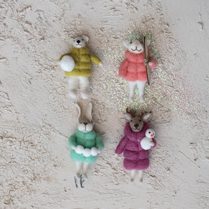 The CREATIVE COOP HANDMADE WOOL FELT ANIMAL IN WINTER PUFFER COAT ORNAMENT set features four animals—rabbit with skates, polar bear with snowboard, reindeer with penguin, and polar bear with snowball—each hanging by a string.