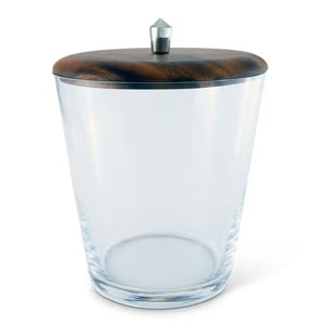 The TRIBECA GLASS ICE BUCKET by VAGABOND HOUSE features a round, transparent body made of clear glass, topped with a dark wooden lid that has a small metallic knob in the center. The bucket stands on a white surface, exemplifying Mid-Century Modern Design and urbane sophistication with its minimalistic and sleek aesthetic.