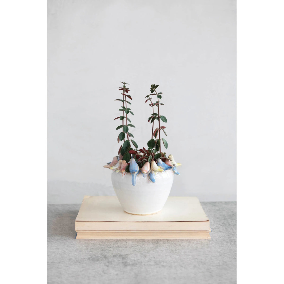 The PLANTER W BIRDS ON RIM by CREATIVE COOP is a ceramic piece made entirely from stoneware, showcasing a smooth, white exterior with small pastel-colored bird sculptures—yellow, pink, and blue—gracefully adorning the rim.