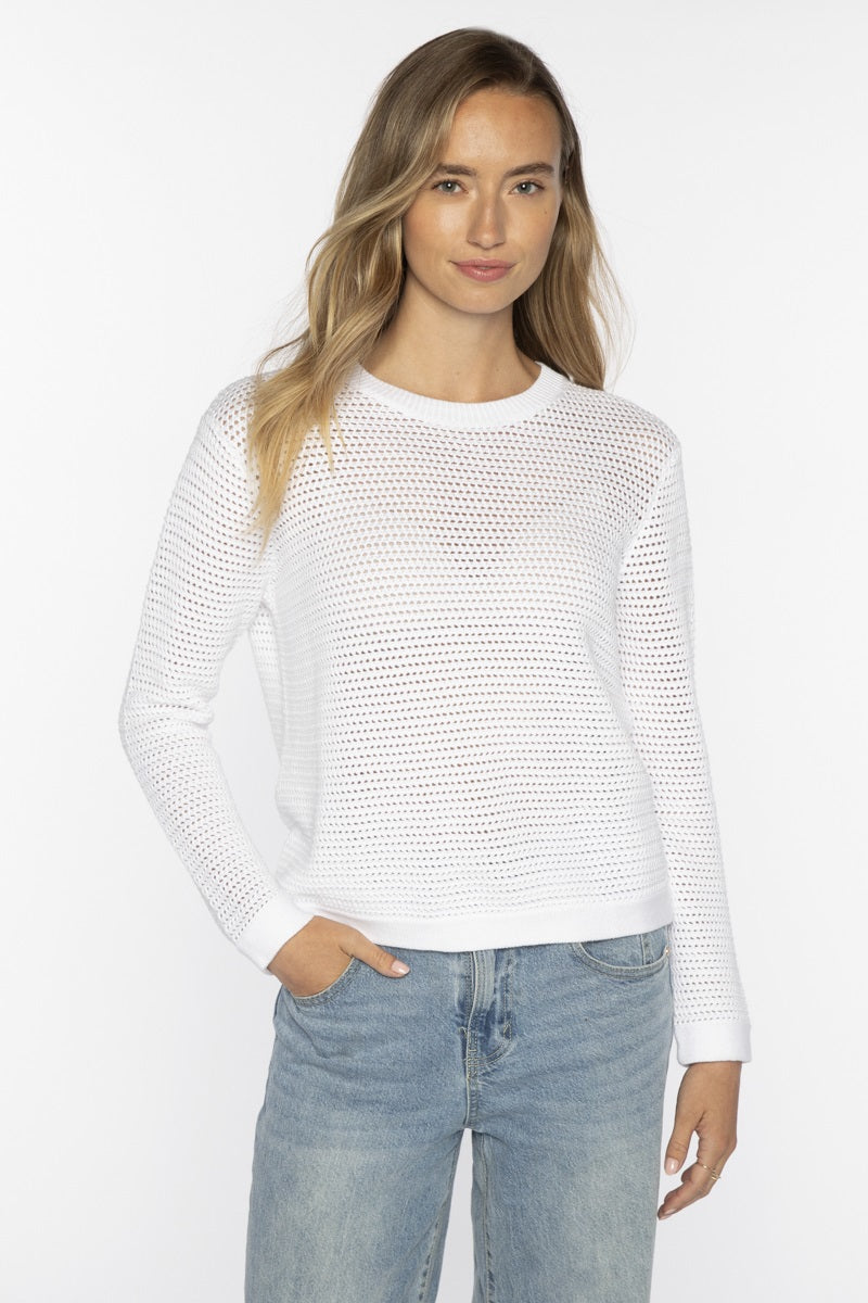 A woman with long, wavy blonde hair wears the KINROSS CASHMERE Openwork Crew Neck Cotton Sweater in Skyway by KINROSS, paired with light blue jeans. She stands against a plain white background and smiles softly.
