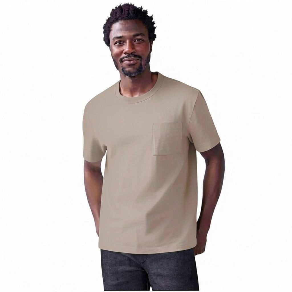 A man with short curly hair and a beard wears the MACK WELDON Heavyweight Slub Cotton Pocket T-Shirt in Desert Taupe and dark pants, standing against a plain white background.