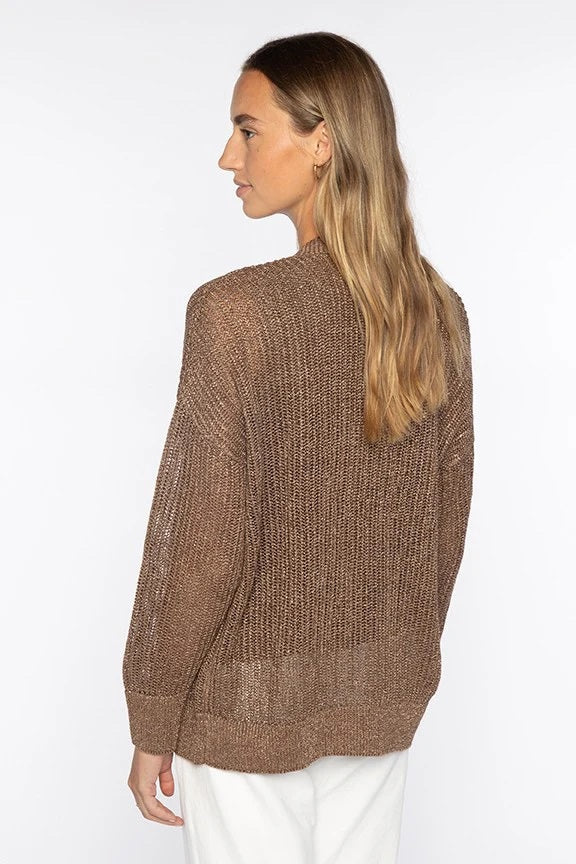A woman with long, light brown hair wears the KINROSS CASHMERE Open Texture Lurex Linen Cardigan over a matching top and white pants. She stands against a white background, one hand in her pocket, smiling softly.