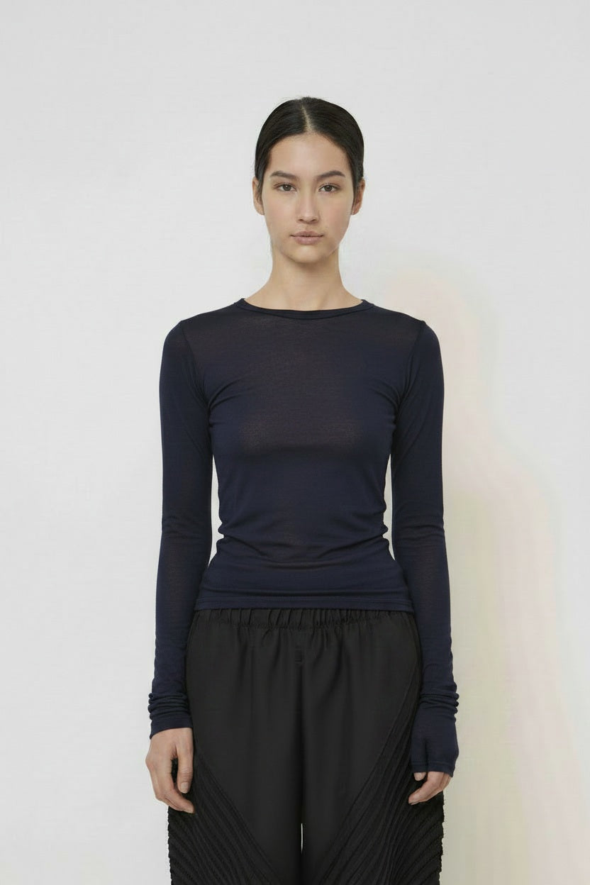A woman with long dark hair in a low ponytail stands in profile against a plain light background, wearing the MEIMEIJ MESH LAYERING TOP by MEIMEIJ in red and a black skirt for a minimalist Italian fashion look.