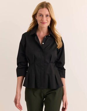 A woman with blonde hair is smiling at the camera while standing against a plain light background, wearing the HINSON WU - MARTINA 3/4 SLEEVE STRETCH POLISHED COTTON SHIRT IN BLACK paired with olive green pants.