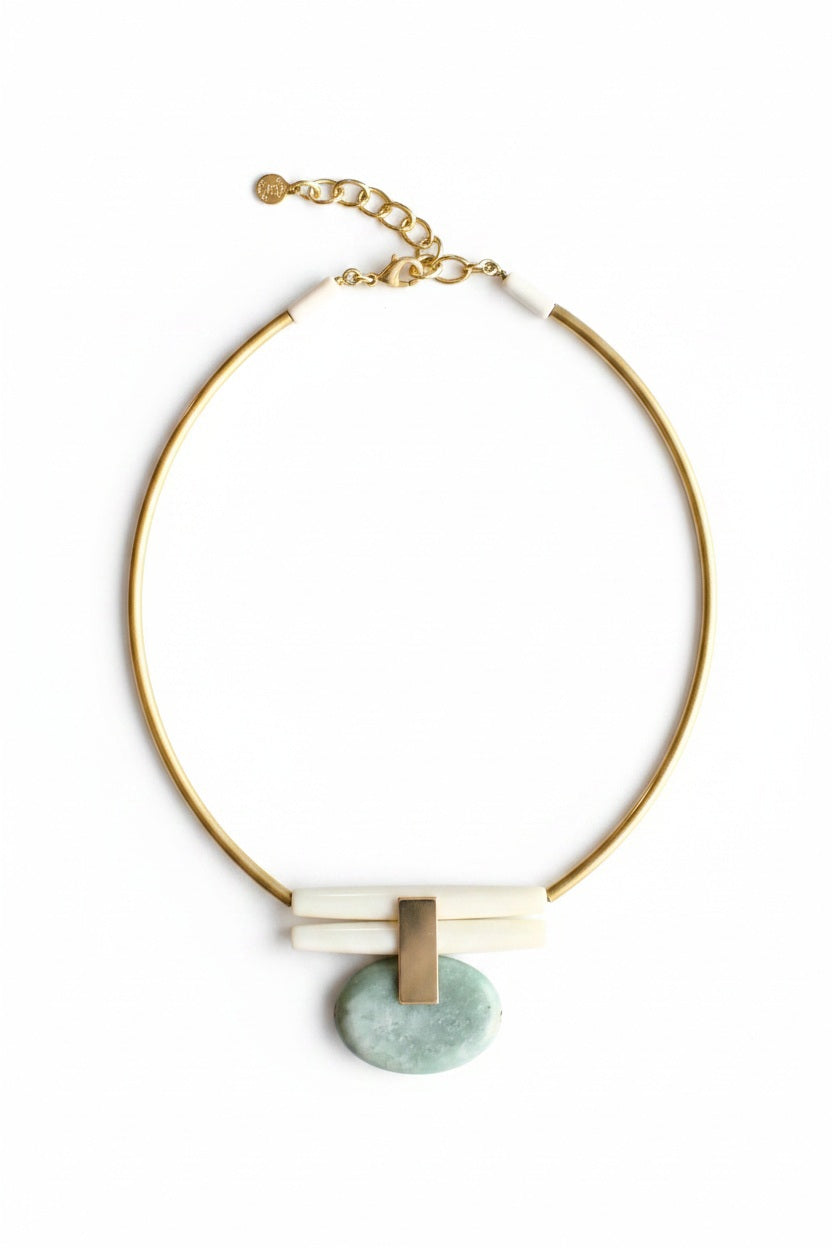The DAVID AUBREY - GREEN JASPER AND BRASS ARTDECO NECKLACE by DAVID AUBREY features a gold chain with a light blue oval stone pendant that evokes the unique look of teal green jasper, complemented by white rectangular accents and an adjustable chain clasp, all presented on a gray background.