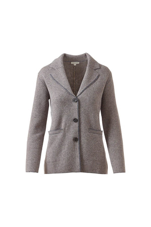 A woman with wavy brown hair wears the KINROSS CASHMERE Herringbone Notch Collar Knit Cardigan under a gray blazer with matching pants, standing against a white background with one hand in her pocket.