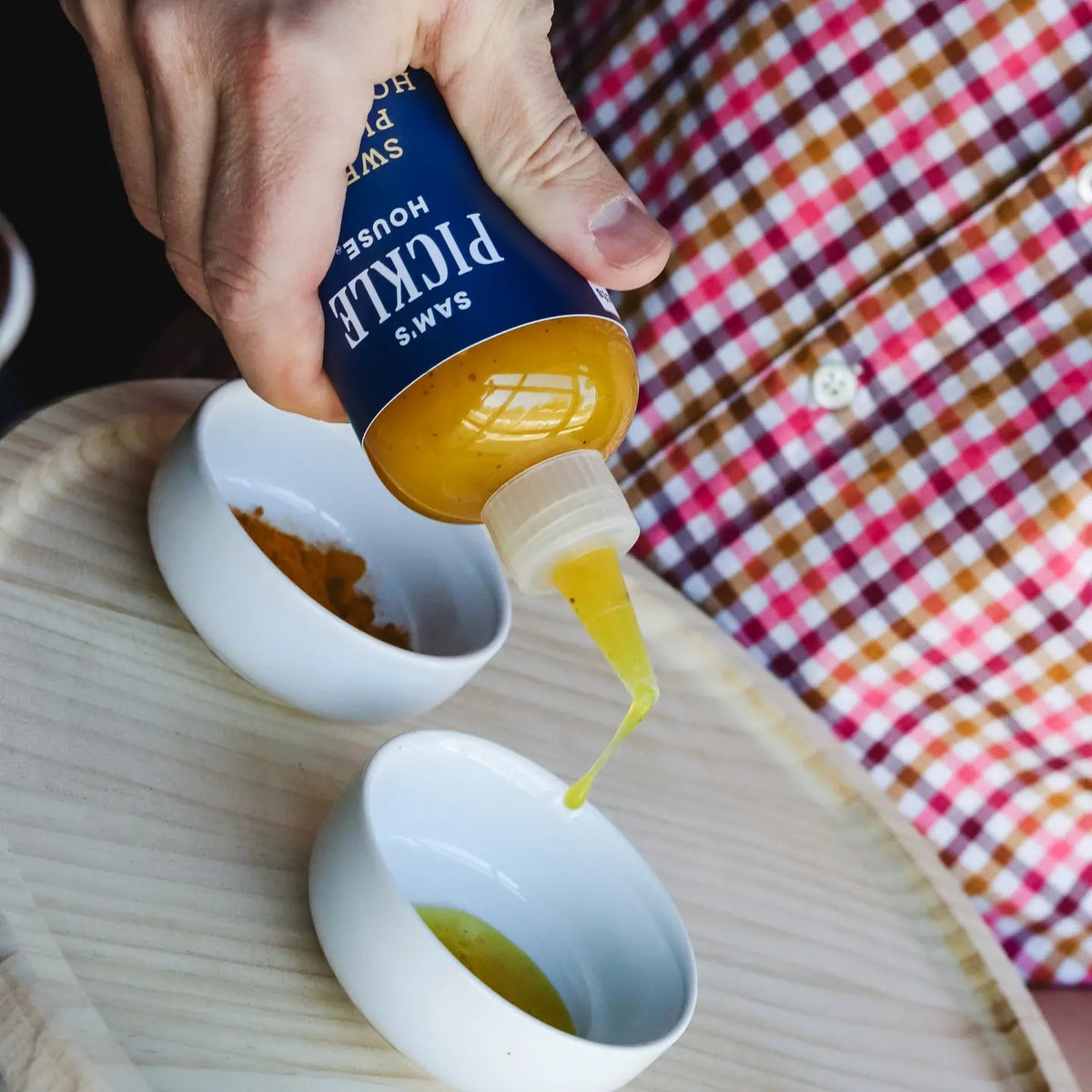 A squeeze bottle labeled “THE PICKLE HOUSE - SWEET PICKLE HOT SAUCE” features a dark blue label with white text. The bottle holds a greenish-yellow, sweet and hot sauce that’s ideal as a salad dressing and comes with a pointed nozzle cap.