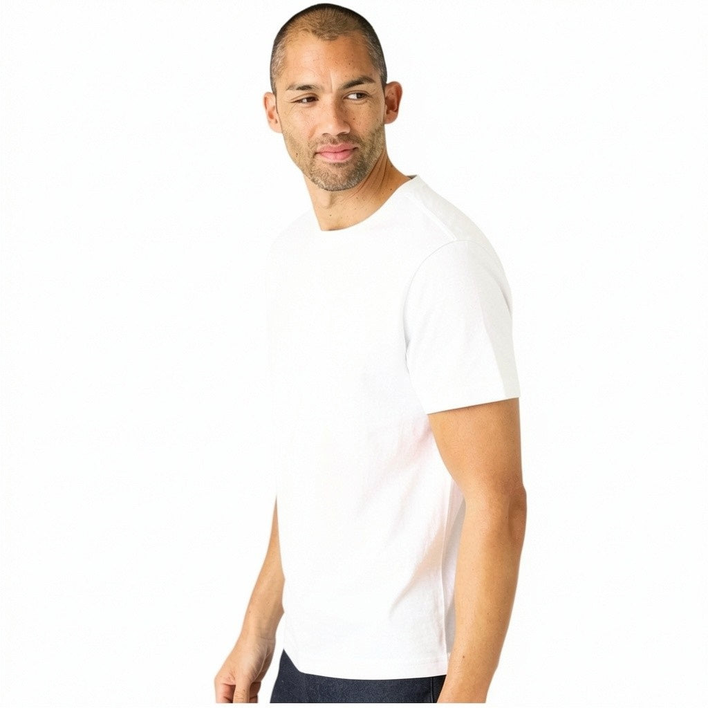 A man with short hair and light stubble wears the MACK WELDON Slub Cotton Crew Neck T-Shirt in Bright White, paired with dark pants, standing against a white background and looking slightly to his left.