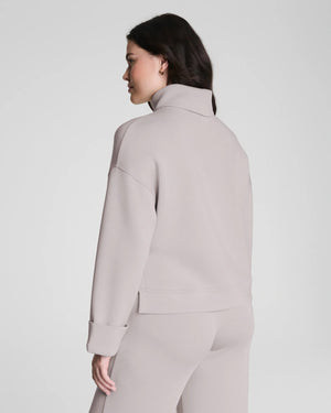 A woman confidently poses in the SPANX - AIRESSENTIALS TURTLENECK TOP and matching pants, crafted from ultra-drapey spacer fabric, against a plain light gray background with a slight smile.