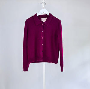 The ROSE & CROWN - CASHMERE CARDIGAN, a luxury long-sleeve button-up in custom-dyed magenta, hangs on a white hanger against a light gray background.