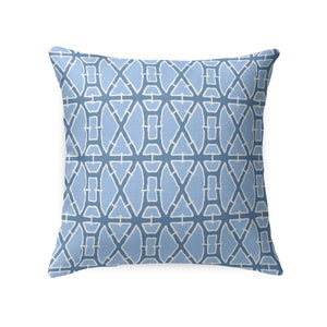 A woven rattan chair with a white cushion and the LOOM AND CLOTH - LATTICE TAILORED PILLOW IN BLUE by LOOM & CLOTH sits next to a white nightstand with vases against a blue floral wallpapered wall.