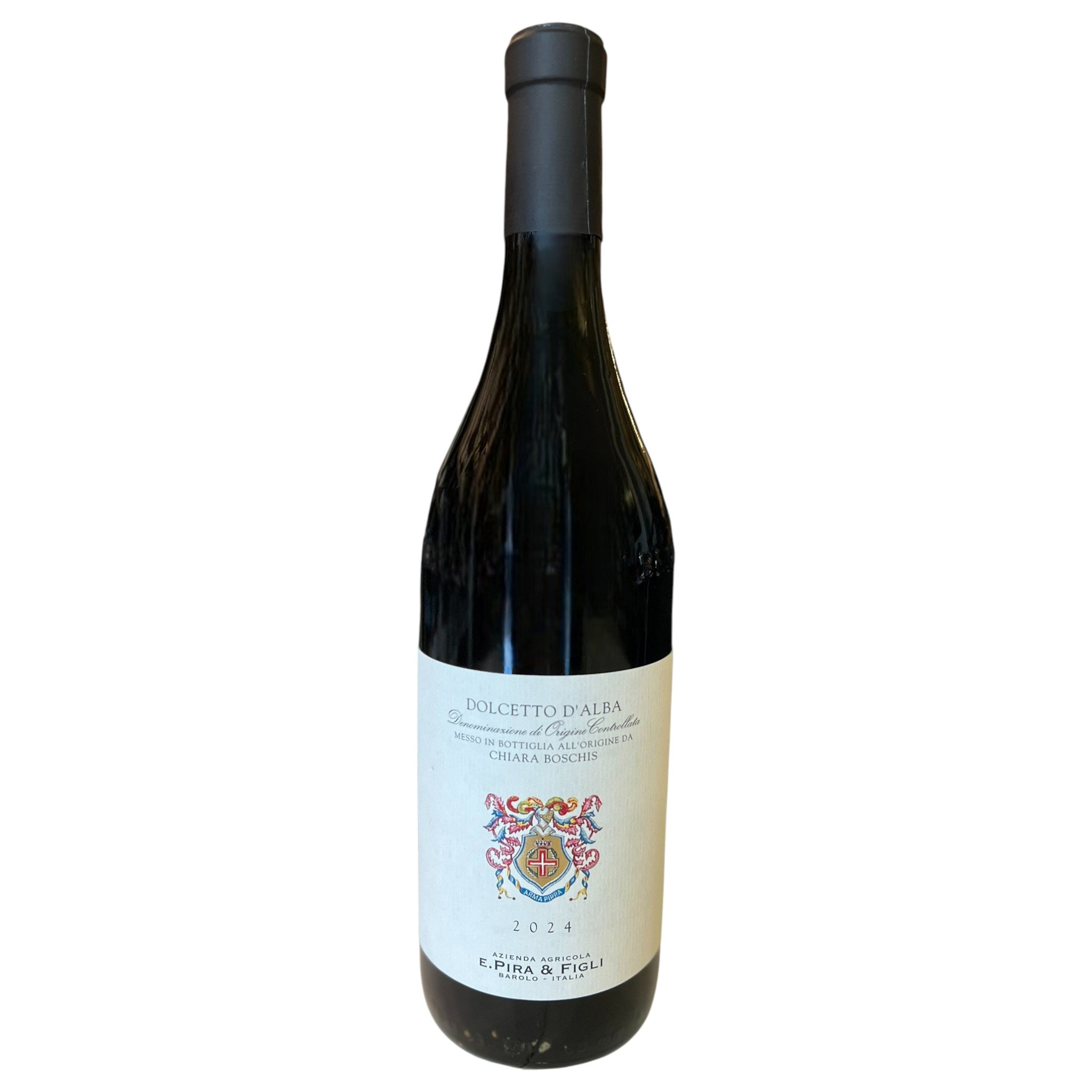 A bottle of E. PIRA DOLCETTO D'ALBA 2024 by WINE: GRAPEVINE, featuring a white label with a decorative crest and text, sits on a light-colored surface with blurred shelves in the background.
