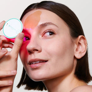 A box labeled “OMNILUX - BLEMISH ERASER HYDROCOLLOID PATCH REFILL KIT” sits beside a round OMNILUX blemish eraser device and a sheet of circular hydrocolloid patches decorated with blue smiley faces and arrows.