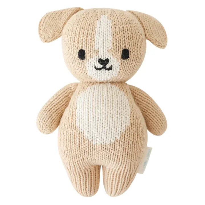 The CUDDLE + KIND - HANDMADE BABY PUPPY by CUDDLE &amp; KIND is displayed from the back, highlighting its beige knitted body, small floppy ears, stubby arms, and short tail with no visible facial details. Meticulously hand-knit from 100% cotton yarn, its texture is distinctly visible, enhancing its cozy and handcrafted appeal. Perfect for those who appreciate fair trade and hand-knit baby animals.