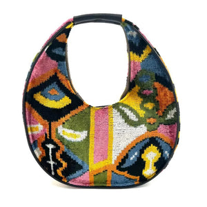 The BALDIZ LUCA Bag in Paloma is a large, crescent-shaped shoulder bag with a black handle and vibrant abstract floral patterns—perfect for everyday use.