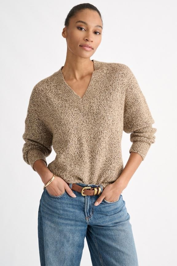 A person wearing the KINROSS CASHMERE Sequin Marle Easy Vee Neck Sweater in Scotch, paired with blue jeans and a brown belt, stands with hands in their pockets against a plain light background.