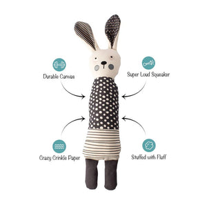 The FRINGE STUDIO - ALL EARS RABBIT CANVAS DOG TOY by PET SHOP BY FRINGE STUDIO is a light-colored fabric doll resembling a rabbit that stands upright. It has long ears, one black and one patterned, with a polka-dot dress combined with striped fabric. Designed for interactive play, the doll features simple facial details with round eyes, a small nose, and pink cheeks.