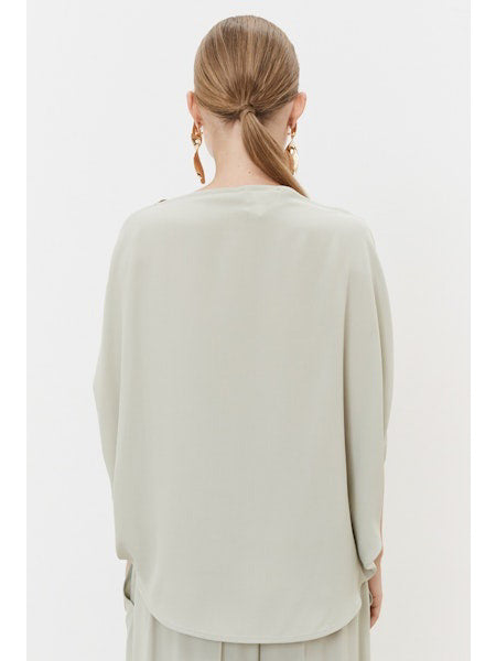A person with tied-back hair faces away, wearing a light gray MEIMEIJ Silk Blend Top with minimalist design and elegant acetate-silk earrings against a plain white background.
