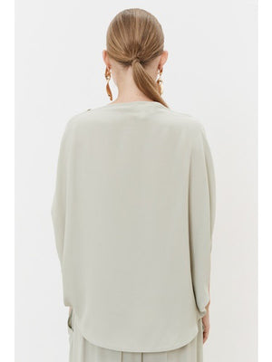 A person with tied-back hair faces away, wearing a light gray MEIMEIJ Silk Blend Top with minimalist design and elegant acetate-silk earrings against a plain white background.
