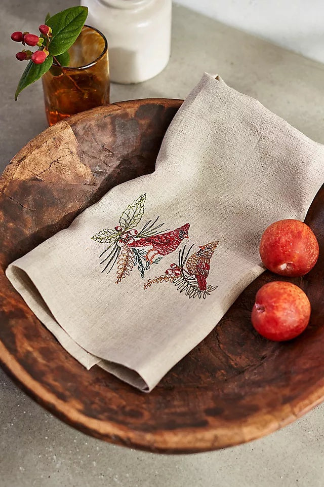 A CORAL & TUSK CHRISTMAS CARDINALS LINEN TEA TOWEL made of embroidered natural flax fiber featuring two cardinals perched on pine branches with berries.