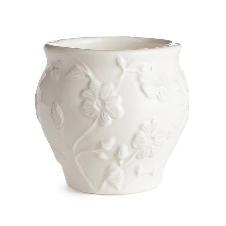 The NAPA HOME AND GARDEN - BLOSSOM CACHEPOT is a white ceramic vase ideal for home decor. It boasts a stunning floral design with embossed leaves and flowers, featuring a rounded shape and slightly flared top edge, reminiscent of a graceful blossom.