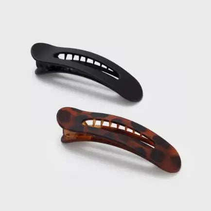 Two sustainable rectangular hair clips, one solid black and the other with a brown and black tortoiseshell pattern, rest on a light pink card. The card emphasizes the recycled materials of "KITSCH - FLAT LAY CLAW CLIP 2 PC," showcasing their style and eco-friendly commitment.