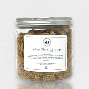 A clear plastic container with a silver lid, labeled "Fearrington Signature Collection - Fearrington Housemade Granola." The label lists ingredients such as oatmeal, sesame seeds, and various nuts. Brimming with gourmet granola, the container is set against a plain white background.