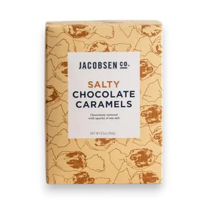 A rectangular box of JACOBSEN SALT CO. CHOCOLATE CARAMELS WITH SEA SALT stands on a light surface, featuring tan packaging with brown abstract patterns and a white label displaying the product name in black and gold.