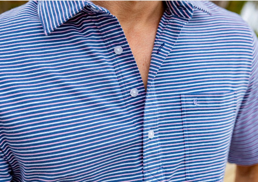 Close-up of a person wearing the CRIQUET Top-Shelf Players Shirt in Stewart Stripe Navy, featuring blue and white stripes, a collar, three buttons, and a small chest pocket. The face is not visible.