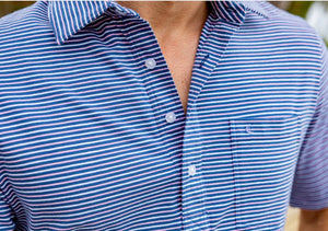 Close-up of a person wearing the CRIQUET Top-Shelf Players Shirt in Stewart Stripe Navy, featuring blue and white stripes, a collar, three buttons, and a small chest pocket. The face is not visible.