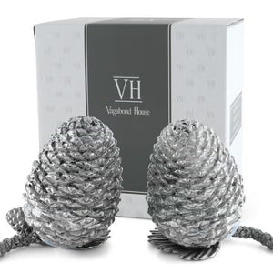 Two detailed silver pine cones stand upright on a white background, resembling the VAGABOND HOUSE - PEWTER PINE CONESALT AND PEPPER SET by VAGABOND HOUSE, with small pine needle segments visible at their bases.