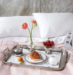A single light pink peony with green leaves in a MATCH - PEWTER FOOTED GLASS VASE by MATCH, partially filled with water and set against a white background.