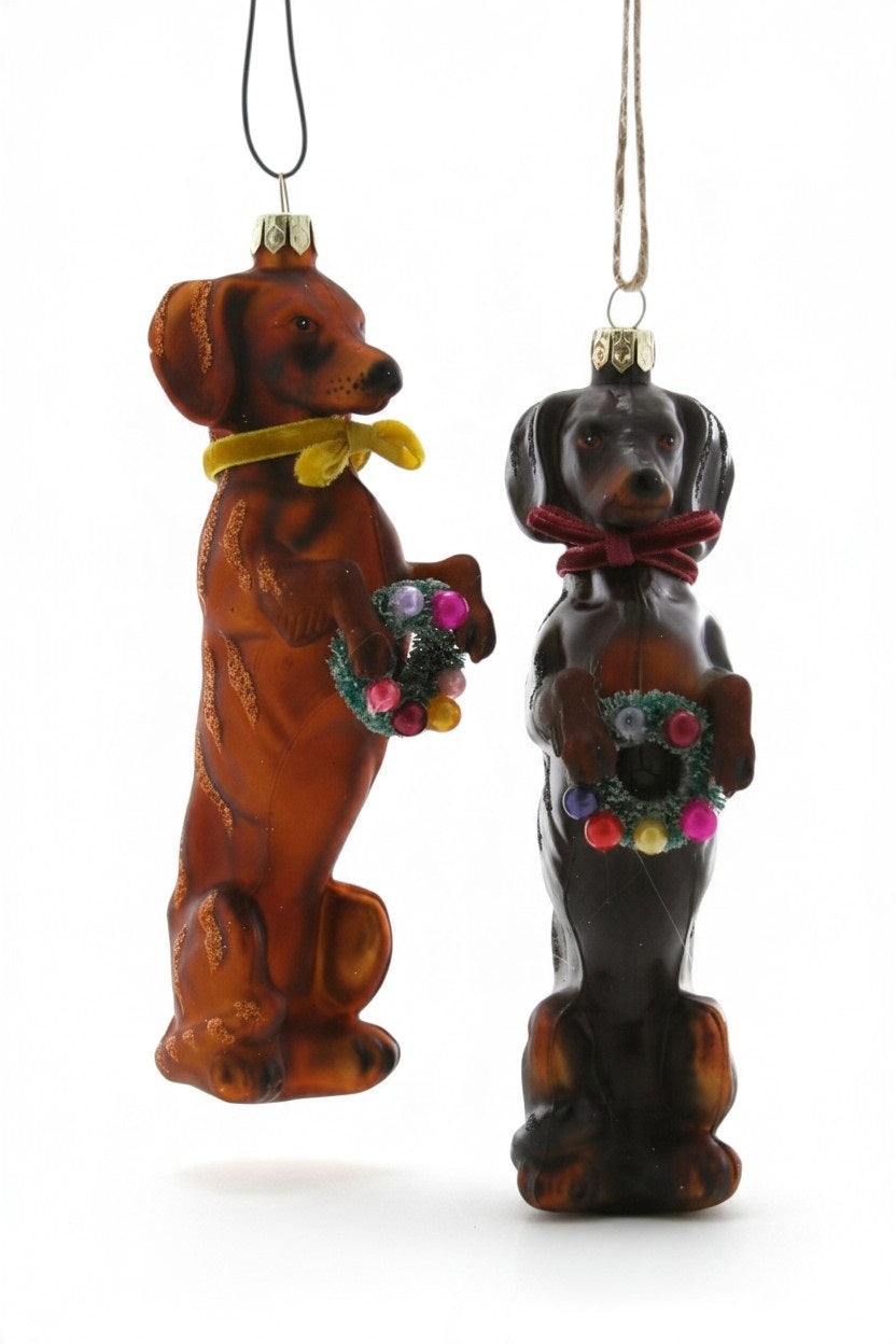 Two 5.75-inch glass FESTIVE DOXY ORNAMENT dachshunds standing on their hind legs, each holding a small festive wreath.