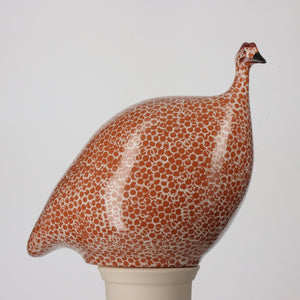 A ceramic sculpture called the "Large Pecking Ceramic Guinea in Red Spotted White" by Les Ceramiques de Lussan, featuring a design reminiscent of French guinea hens with a speckled white and orange pattern. It showcases a small head with a short beak, mounted on a light-colored cylindrical base against a plain background.