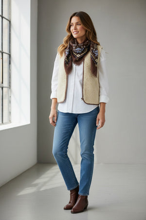 The STORIATIPIC - NELLY wool bandana scarf with embroidery in chocolate is crafted from a soft cashmere blend and features blue, yellow, and beige paisley and geometric patterns with frayed edges. Displayed folded in a triangle shape against a plain white background, this accessory highlights the distinctive style of the STORIATIPIC brand.
