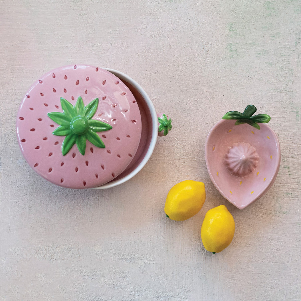 Two views of the HAND-PAINTED STONEWARE STRAWBERRY SHAPED JUICER by CREATIVE COOP: a unique artisan piece with pink strawberry design and green leaves, shown from both the top and side—perfect kitchen decor for fruit lovers.