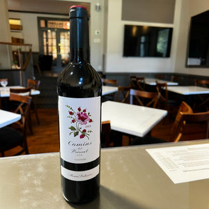 A bottle of ALVARO PALACIOS ‘CAMINS DEL PRIORAT’ 2024 red wine from WINE: ADVINTAGE, featuring a white label adorned with a floral illustration and the text “Camins del Priorat 2024” and “Product of Spain.” Crafted by acclaimed winemaker Álvaro Palacios, this Garnacha blend is elegantly finished with a dark foil around the neck.