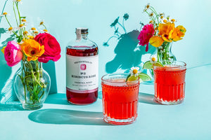 A transparent glass bottle holds a rich, dark red liquid labeled "YES COCKTAIL CO - Hibiscus Rose Cocktail Mixer." Handcrafted in California and available in a 16 fl oz (473ml) size, the white-and-red-toned label indicates its perfect suitability for creating cocktails or an exotic floral spritzer.