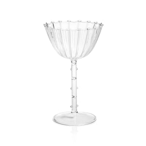 The ZODAX CHAUMONT Coupe Glass (260 ml), crafted from clear fluted Borosilicate glass, sits on a reflective silver tray with a metallic vase and wine bottle softly blurred in the background against a neutral surface.