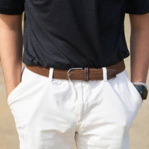 The ROOSTAS - MOJAVE WOVEN STRETCH BELT features a brown woven design, silver buckle, dark brown leather accents with white stitching, and an adjustable clasp for comfort. Coiled with the buckle facing left. Brand: ROOSTAS.