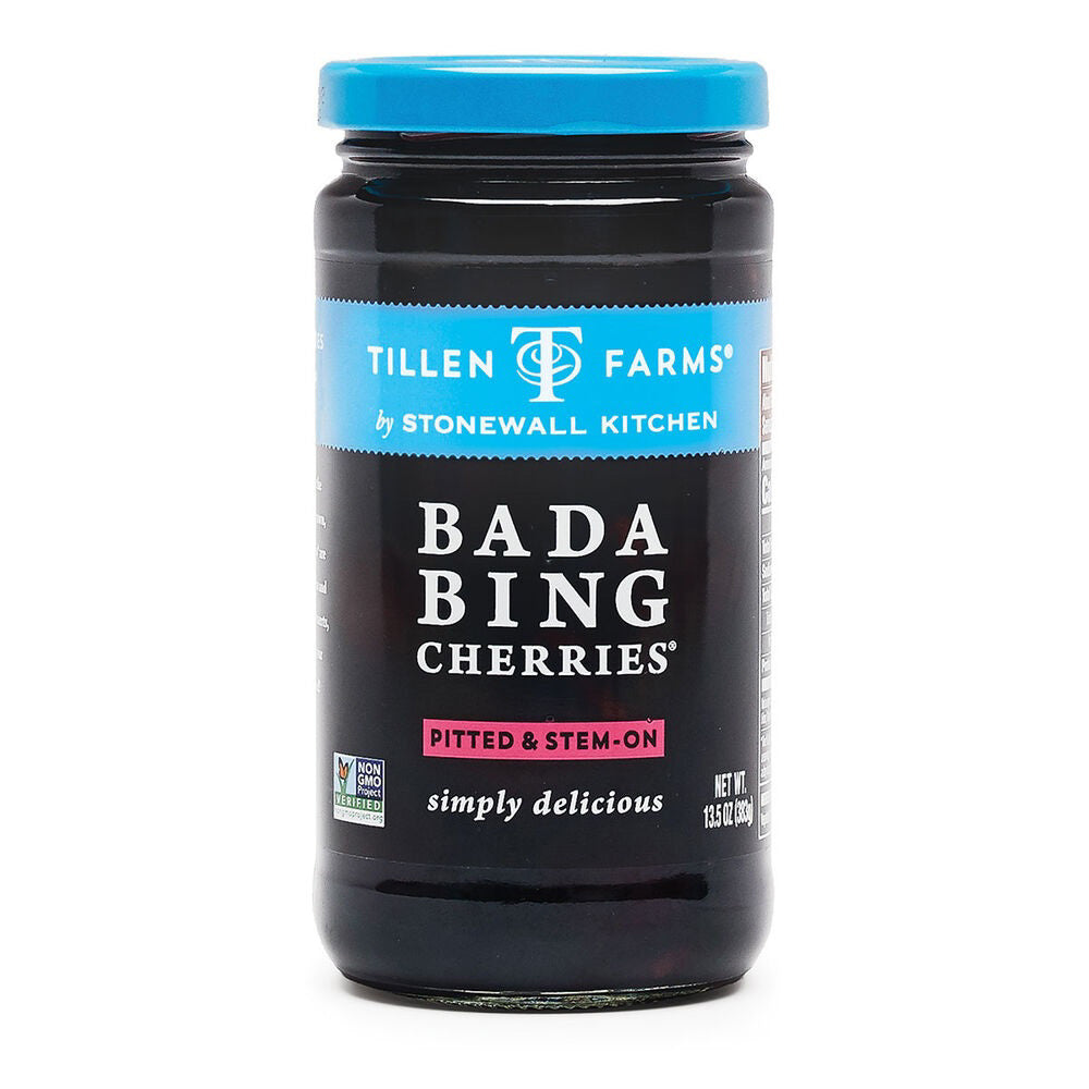 A jar of Stonewall Kitchen Bada Bing Cherries features a black label with white and blue text, proudly displaying "Non-GMO certified." The cherries, ideal for cocktails or snacking, are pitted and stem-on. The bottom of the jar reads "simply delicious," with a net weight of 13.5 oz (383g).